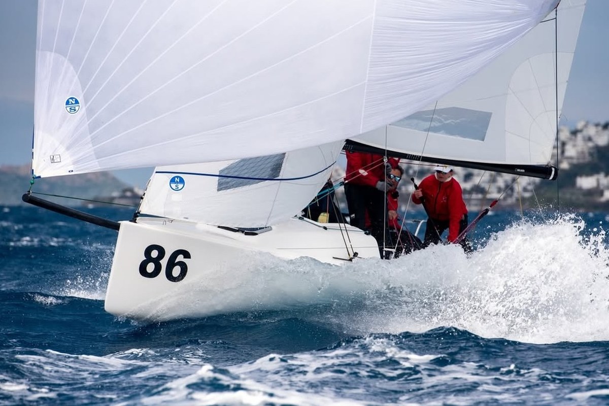 J/70 hull 86 driving hard through spray, crew in red